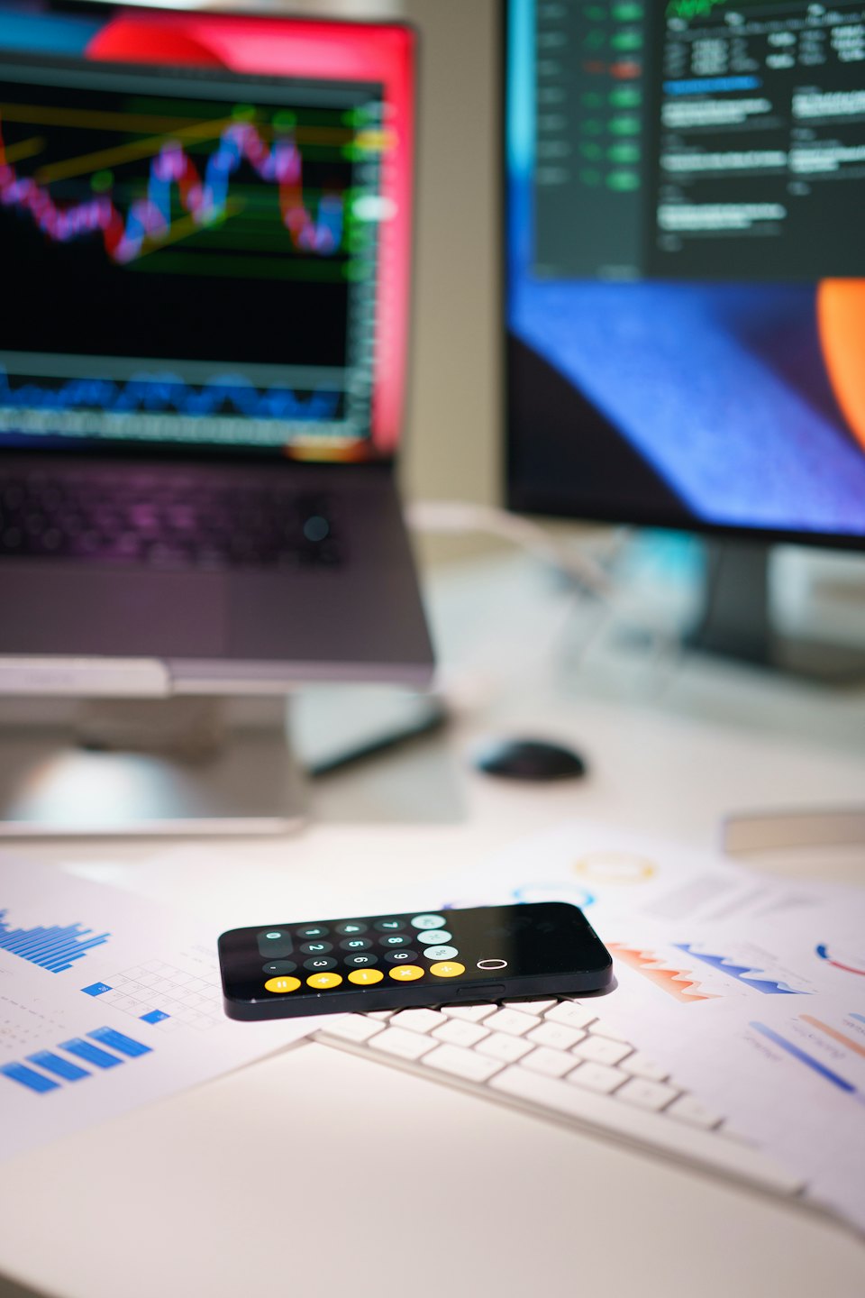 Smartphone su documenti finanziari vicino a un laptop con grafici azionari.