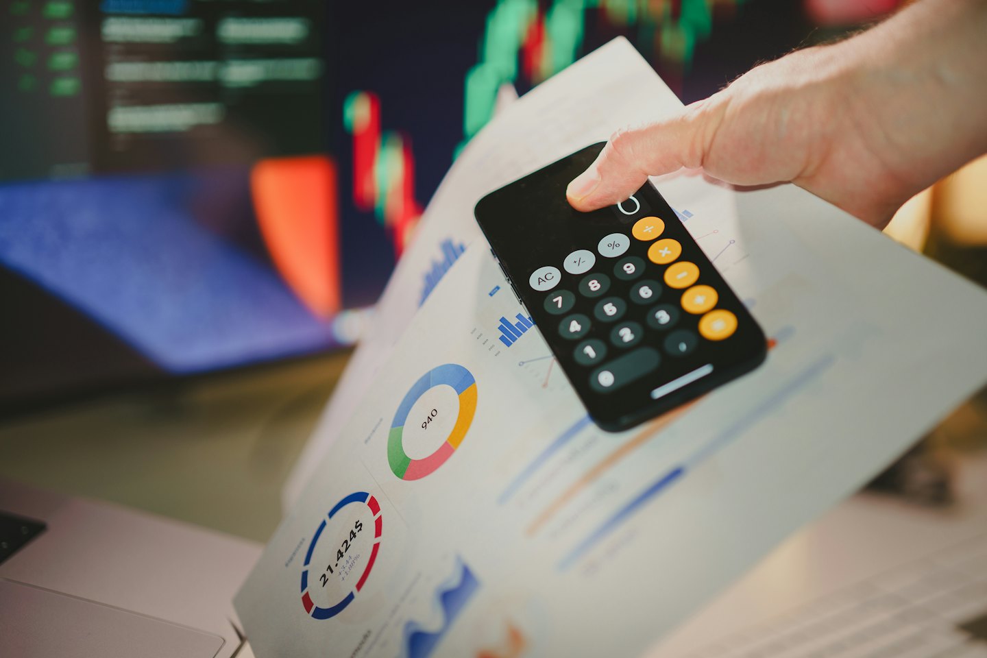 Mano che tiene uno smartphone sopra documenti finanziari e grafici.